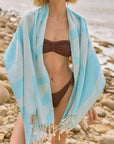 Light blue Turkish towel draped over a woman on a rocky beach, lightweight and quick-drying.