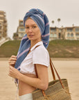 Lane Turkish towel in Lilac Green – walking away from beach with towel on head and straw bag