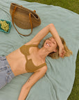 Woman relaxing on a sage green blanket on the grass with a woven bag and grapes beside her, lightweight and breathable.