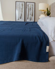 Blue textured blanket on a bed with a lamp and decor in the background