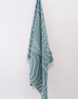 Teal towel with white patterns hanging on a white wall