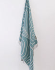 Teal towel with white patterns hanging on a white wall