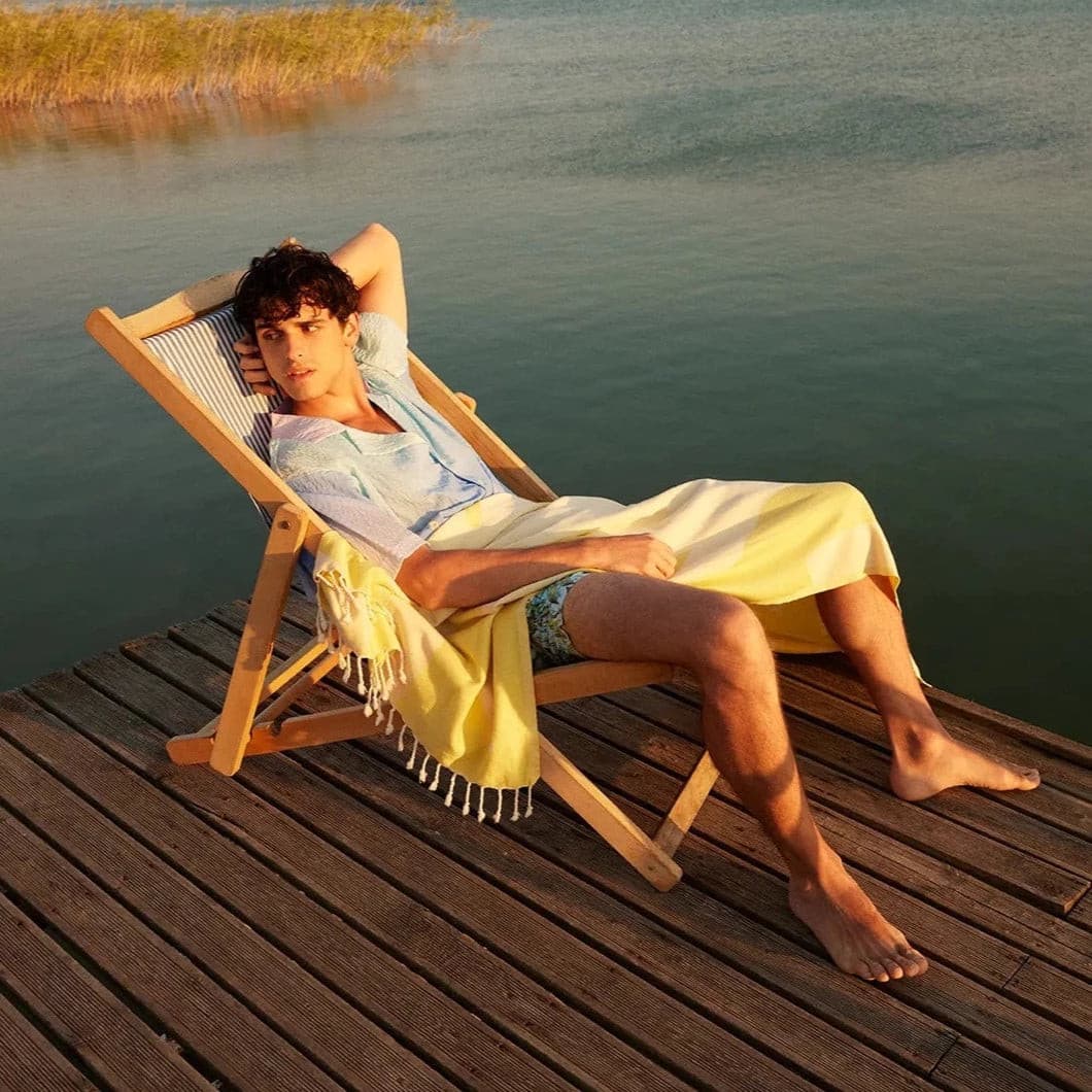 Fiori Turkish towel in Mellow Yellow – draped over lounging man on dock at lakeside, summer evening glow