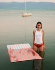 Lane Turkish towel in Peach Cream – floating on lake surface next to model with sailboat in background, towel absorbing water