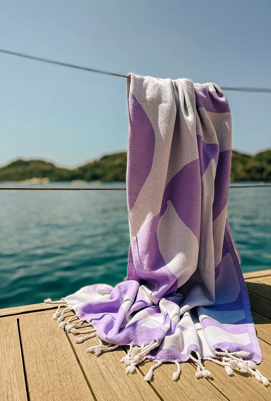 Fiori Turkish towel in Lilac – hanging on dockside rope overlooking a calm bay