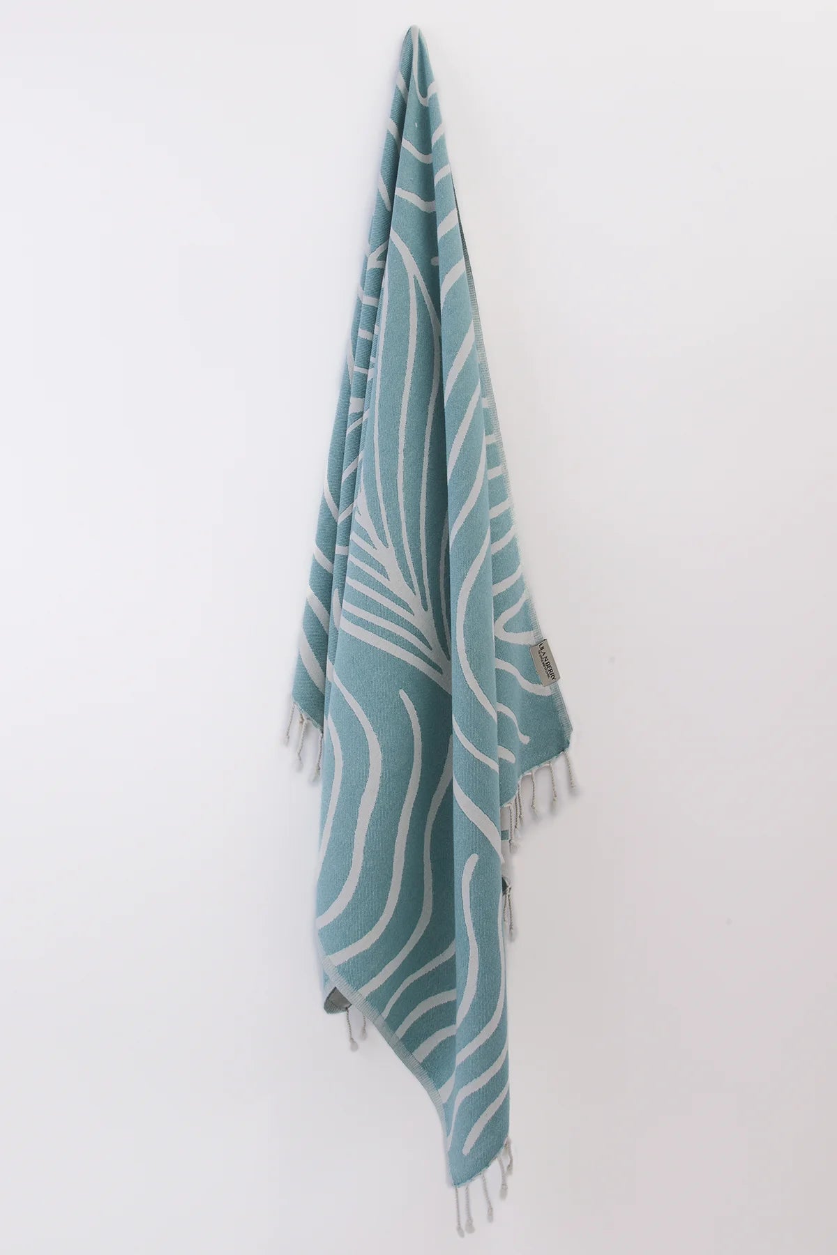 Teal towel with white patterns hanging on a white wall