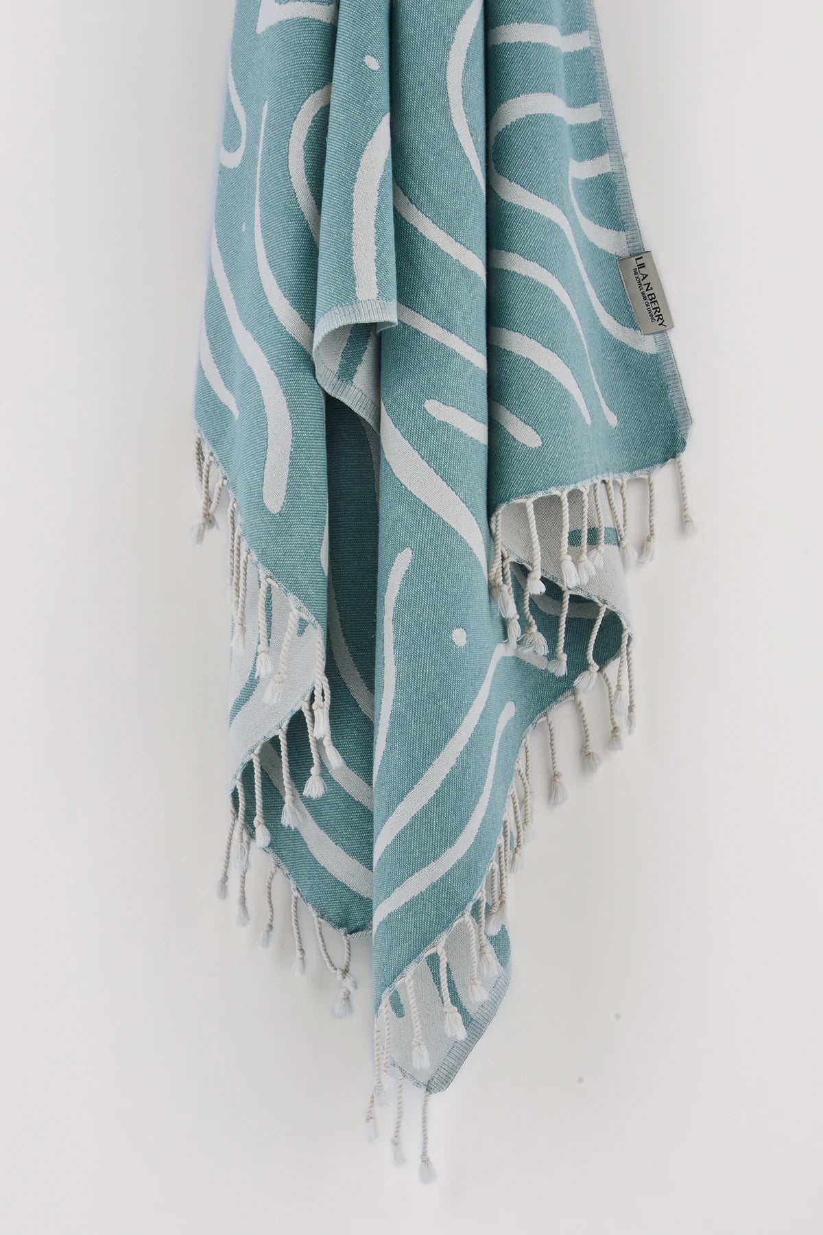 Teal and white patterned towel with fringes on a white background